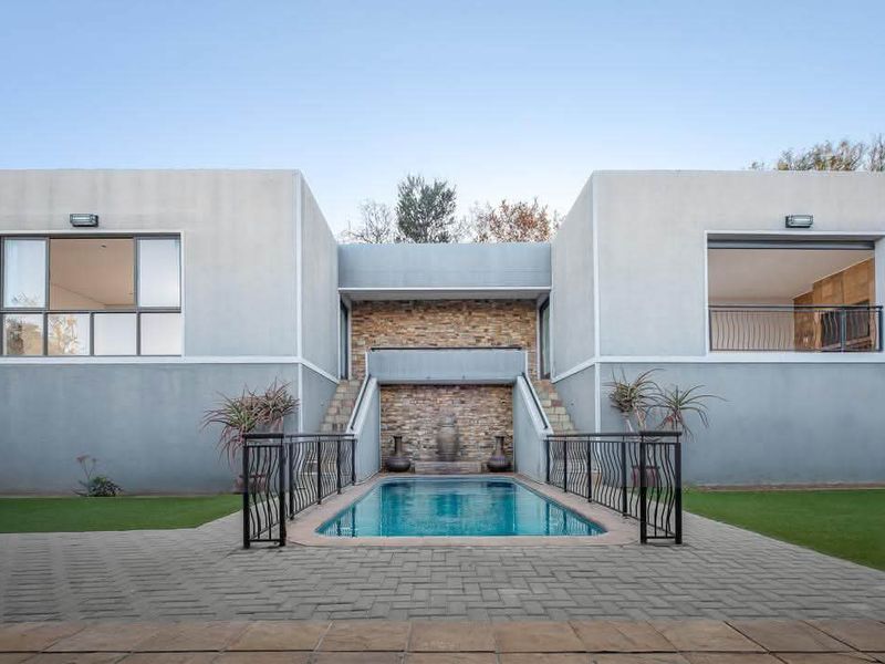 A modern rear exterior featuring a swimming pool, stone-clad water feature, paved patio area, and dual-wing building structure with balcony access.