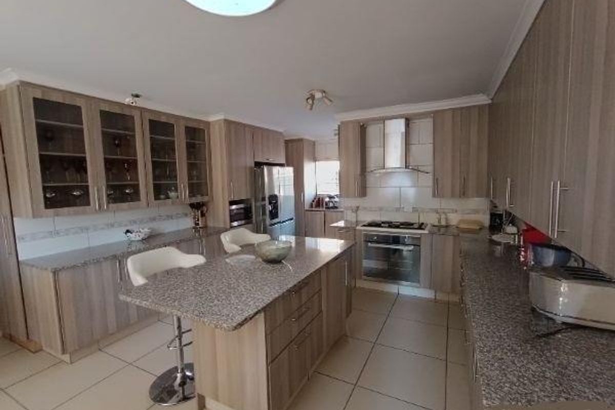Modern kitchen featuring granite countertops, a central island with breakfast bar, stainless steel appliances, and ample built-in cabinetry with glass-fronted display units.