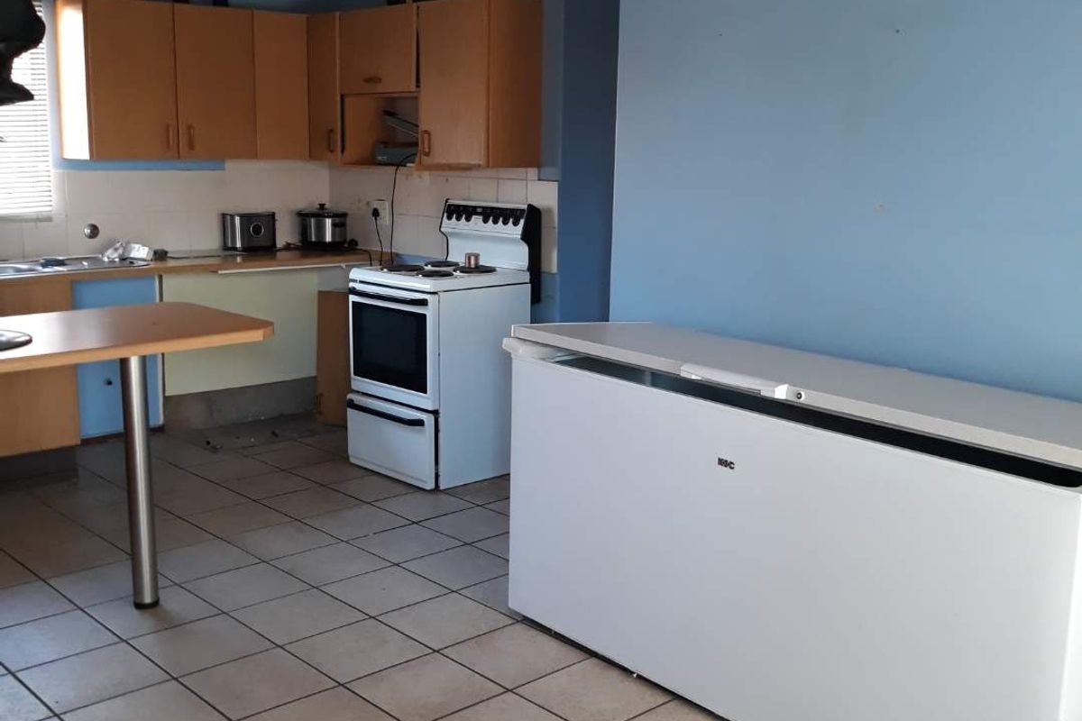 A dated kitchen featuring wood-tone cabinetry, tiled flooring, and a freestanding stove, offering significant potential for a modern renovation and aesthetic update.