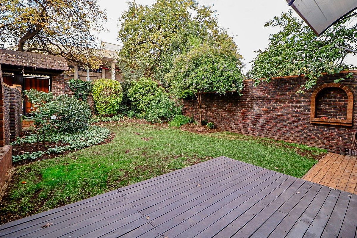 A private rear garden featuring a timber deck, established trees, and a classic brick boundary wall with a decorative arched niche.