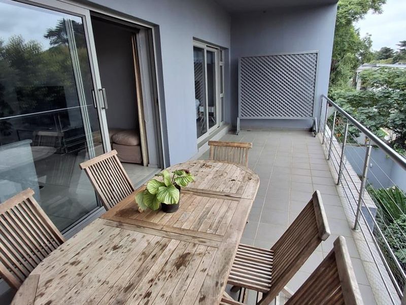 A spacious covered balcony featuring tiled flooring, a metal balustrade, and sliding glass door access to the interior living area.