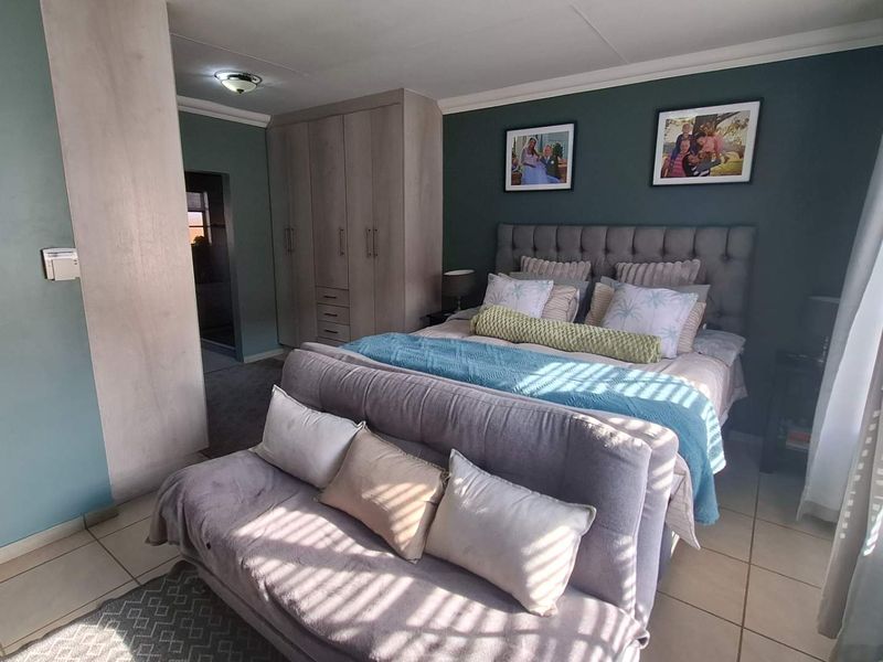 A well-maintained bedroom featuring built-in cupboards, tiled flooring, and a neutral color palette with a feature wall.