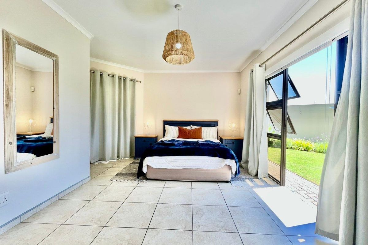 Spacious bedroom featuring neutral tiled flooring, a modern pendant light fixture, and large glass sliding doors providing direct access to the garden.