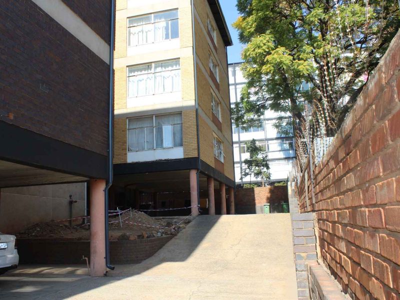 Rear exterior view of the apartment building showing a concrete driveway, brick boundary wall, and ground-level stilt structure with ongoing site maintenance.