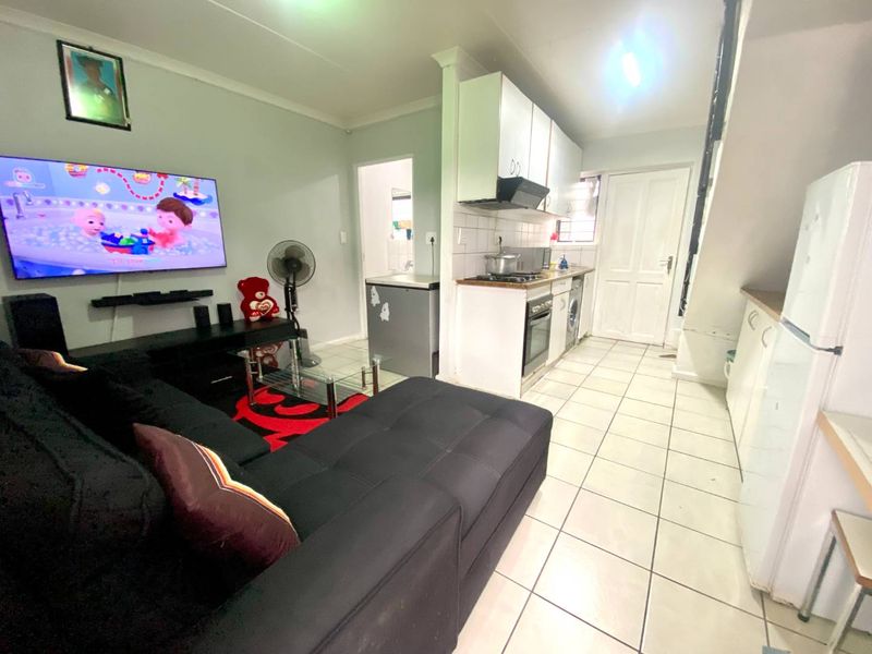 Open-plan living area featuring a compact kitchen with built-in cabinetry, oven, and hob, seamlessly connected to the main living space with tiled flooring throughout.
