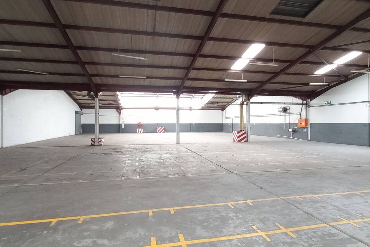 Spacious industrial warehouse featuring high ceilings, exposed steel trusses, concrete flooring, and ample natural light through skylights.
