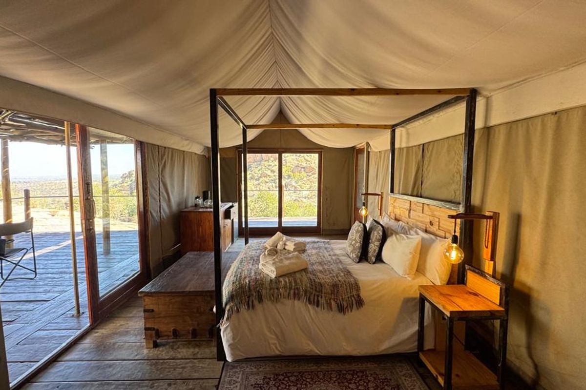 A luxury lodge bedroom featuring canvas walls and ceiling, timber flooring, and large sliding glass doors opening onto a private deck with scenic views.