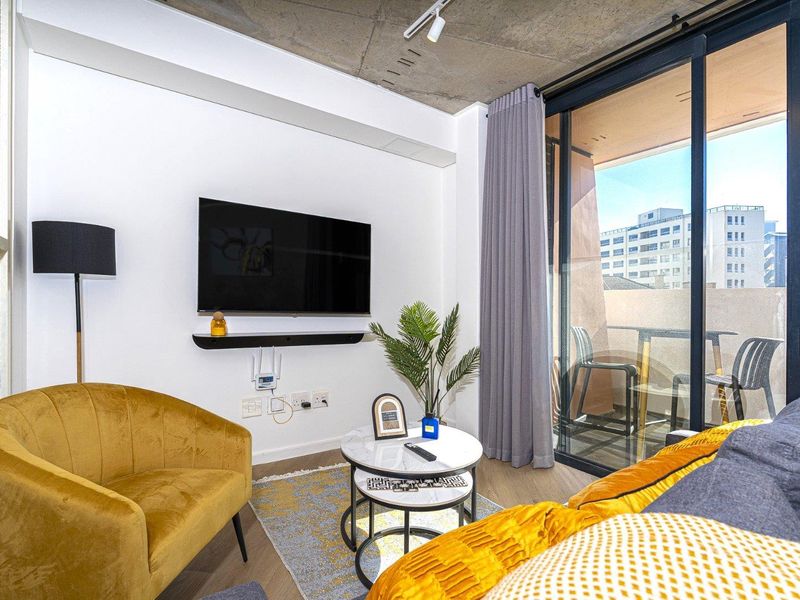 Modern living room featuring an exposed concrete ceiling, track lighting, and large sliding glass doors providing access to the balcony.
