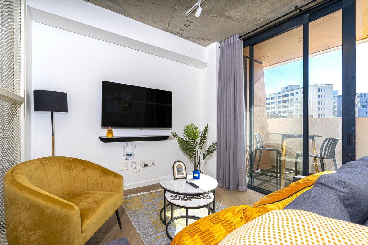 Modern living room featuring an exposed concrete ceiling, track lighting, and large sliding glass doors providing access to the balcony.