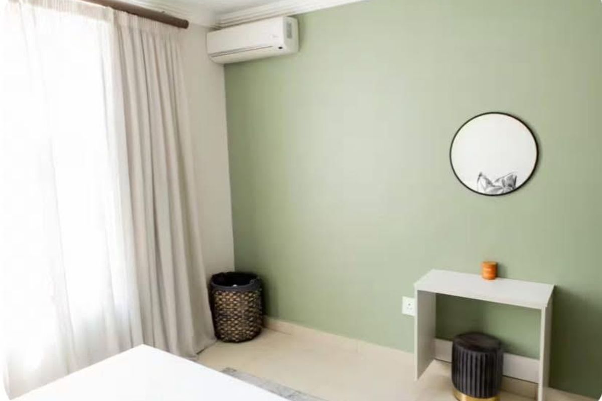 A bedroom featuring a wall-mounted air conditioning unit, tiled flooring, and a large window with curtain tracks.
