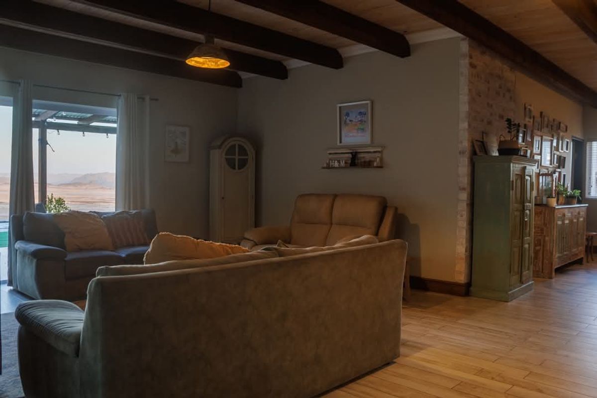 Spacious living area featuring exposed timber ceiling beams, tiled flooring, and a brick feature wall, with direct access to an outdoor patio area.