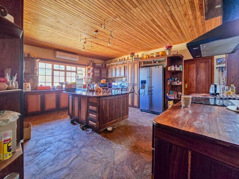 Spacious rustic kitchen featuring extensive wooden cabinetry, a central island, stone flooring, and a timber-clad ceiling, offering a warm and traditional aesthetic.