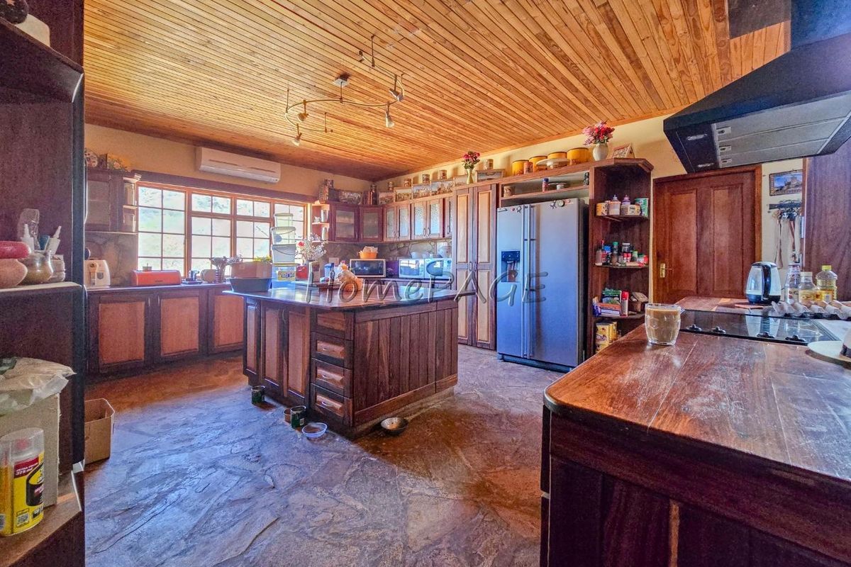 Spacious rustic kitchen featuring extensive wooden cabinetry, a central island, stone flooring, and a timber-clad ceiling, offering a warm and traditional aesthetic.