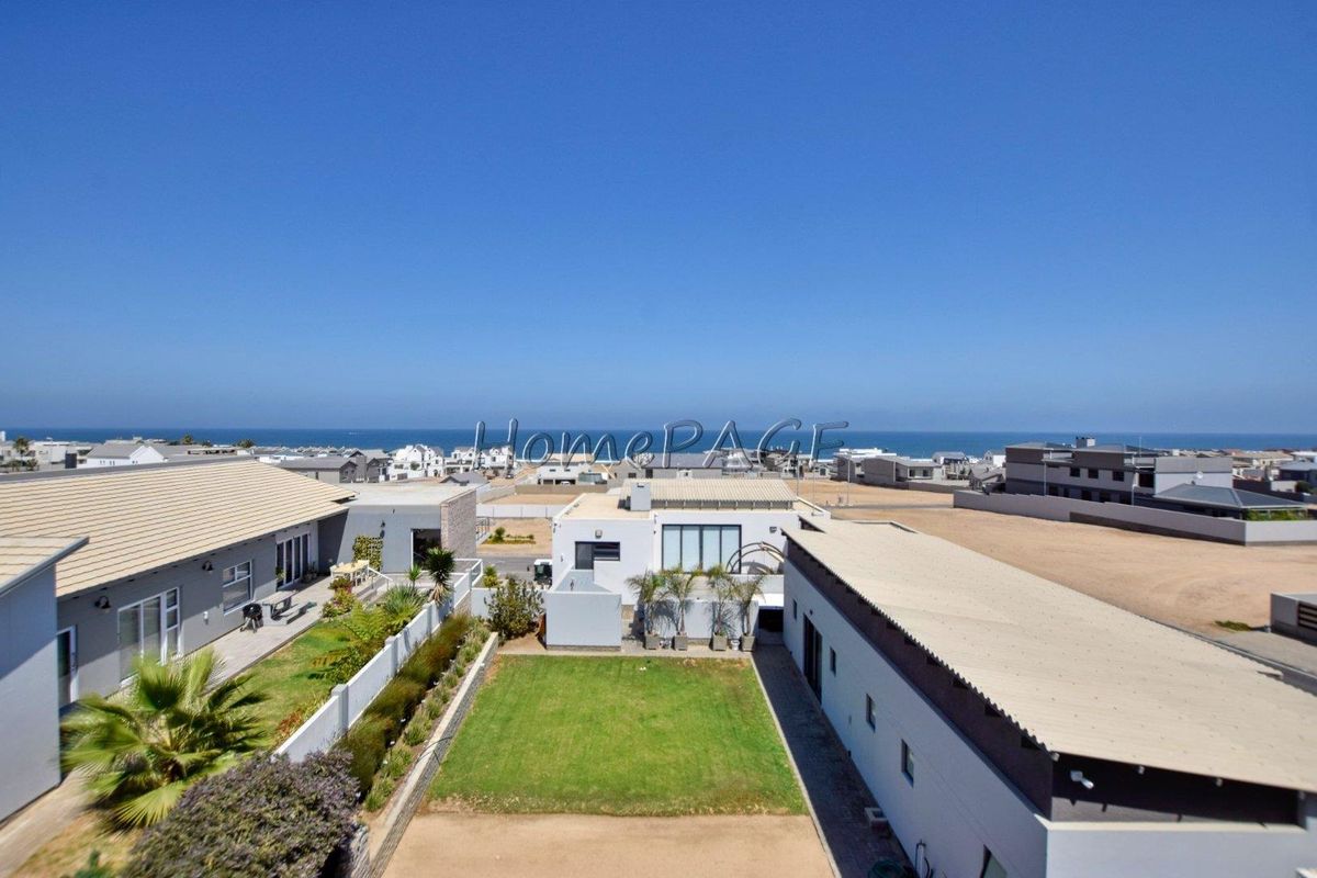 Elevated aerial view of the property featuring a well-maintained lawn, surrounding residential structures, and a clear view of the distant coastline.