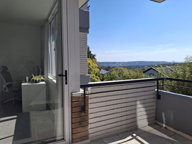 A private balcony featuring tiled flooring, a metal balustrade, and a brick wall, offering elevated views of the surrounding neighborhood.