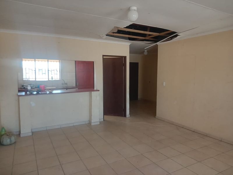 Open plan living area featuring tiled flooring and a breakfast bar, currently requiring ceiling repairs.