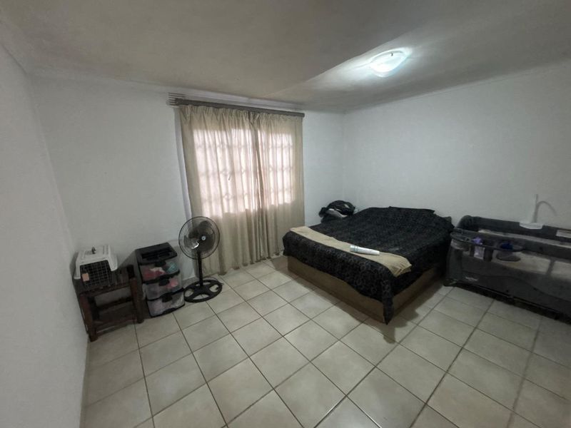 A bedroom featuring tiled flooring and a window with curtain rod. The room requires cosmetic updates to improve its overall condition and appeal.