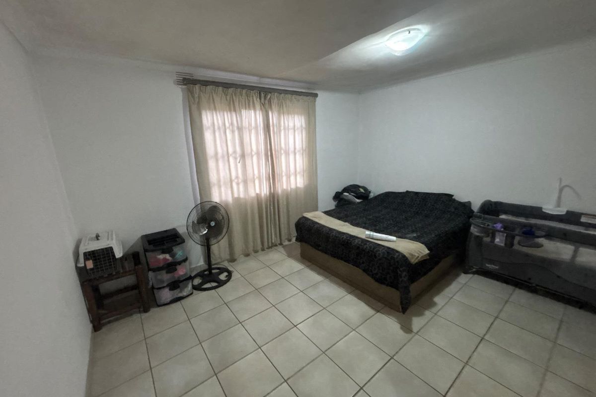 A bedroom featuring tiled flooring and a window with curtain rod. The room requires cosmetic updates to improve its overall condition and appeal.