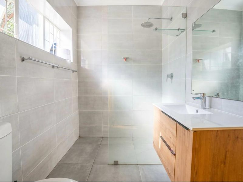 Modern bathroom featuring a walk-in shower with glass screen, contemporary vanity with basin, and neutral floor-to-ceiling tiling.