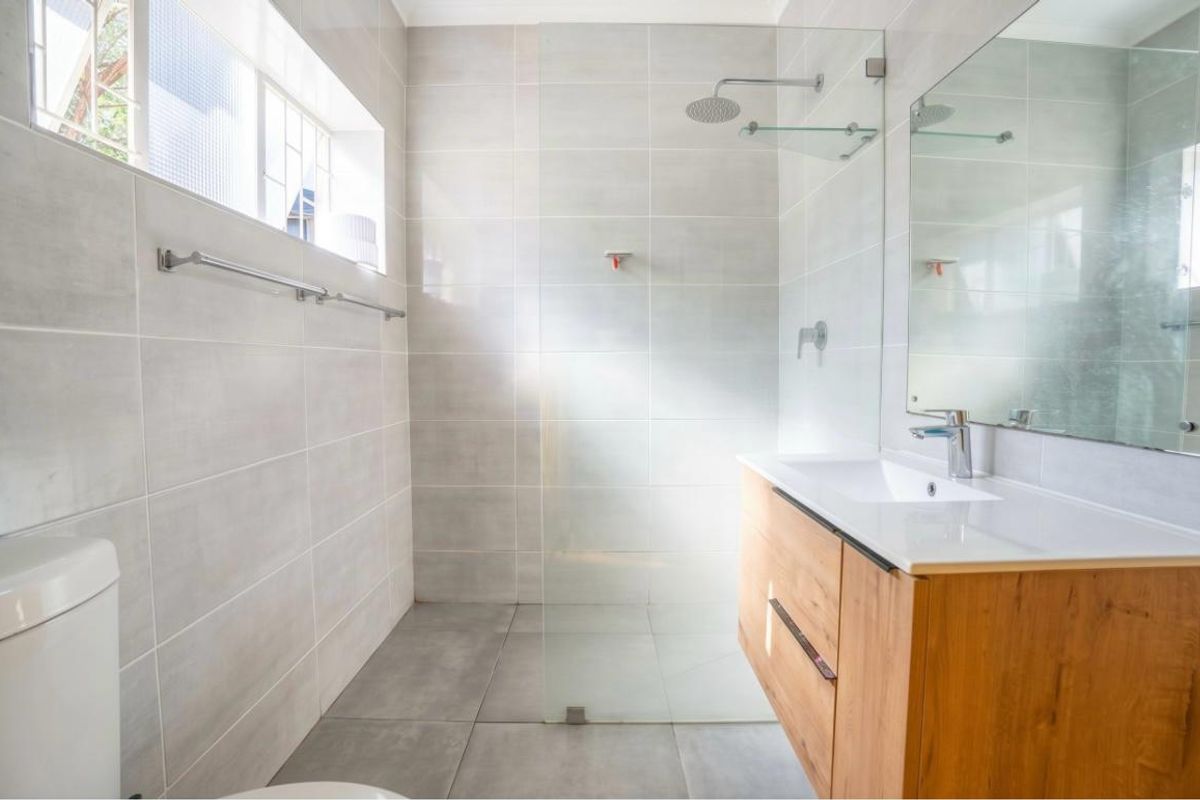 Modern bathroom featuring a walk-in shower with glass screen, contemporary vanity with basin, and neutral floor-to-ceiling tiling.