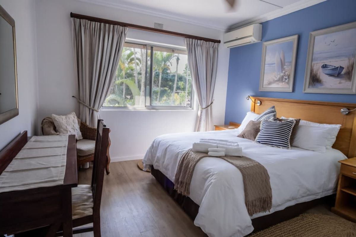 A well-maintained bedroom featuring laminate flooring, an integrated air conditioning unit, and a large window with garden views.