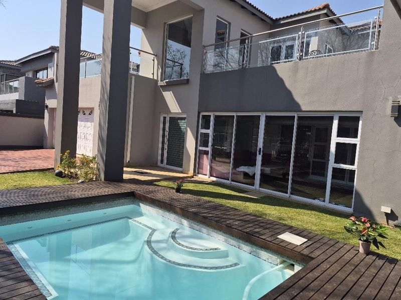 Rear view of the townhouse featuring a swimming pool with timber decking, a spacious upper balcony with glass balustrades, and large sliding glass doors.