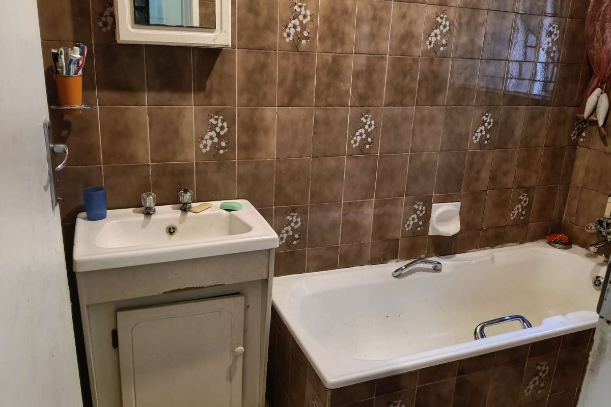 A dated bathroom featuring a vanity cabinet, ceramic basin, and a bathtub with brown patterned wall tiles.