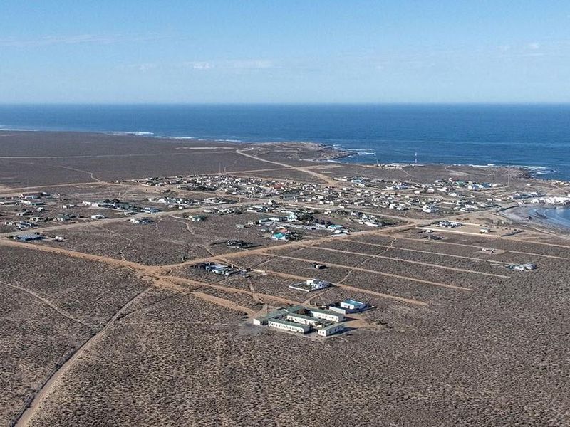 An aerial view of a coastal residential settlement situated in a vast, undeveloped landscape near the ocean.