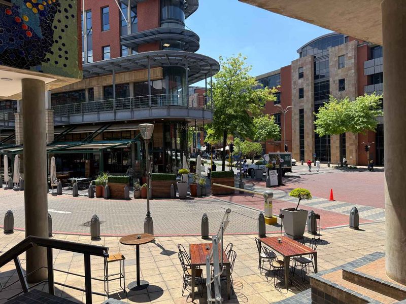 A view of a modern commercial office complex courtyard featuring paved outdoor seating areas, stone pillars, and contemporary brick and glass architecture.