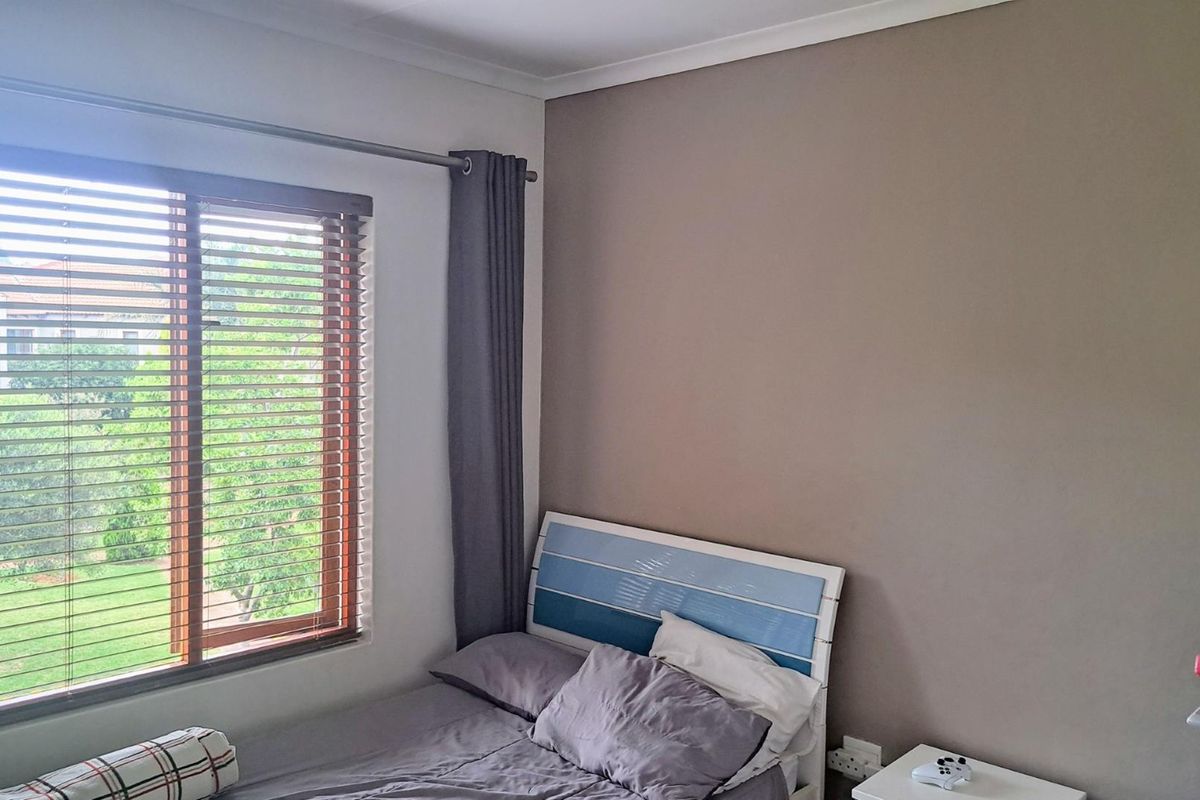 A bedroom featuring a large window with fitted wooden blinds, neutral wall tones, and coved ceiling detailing.