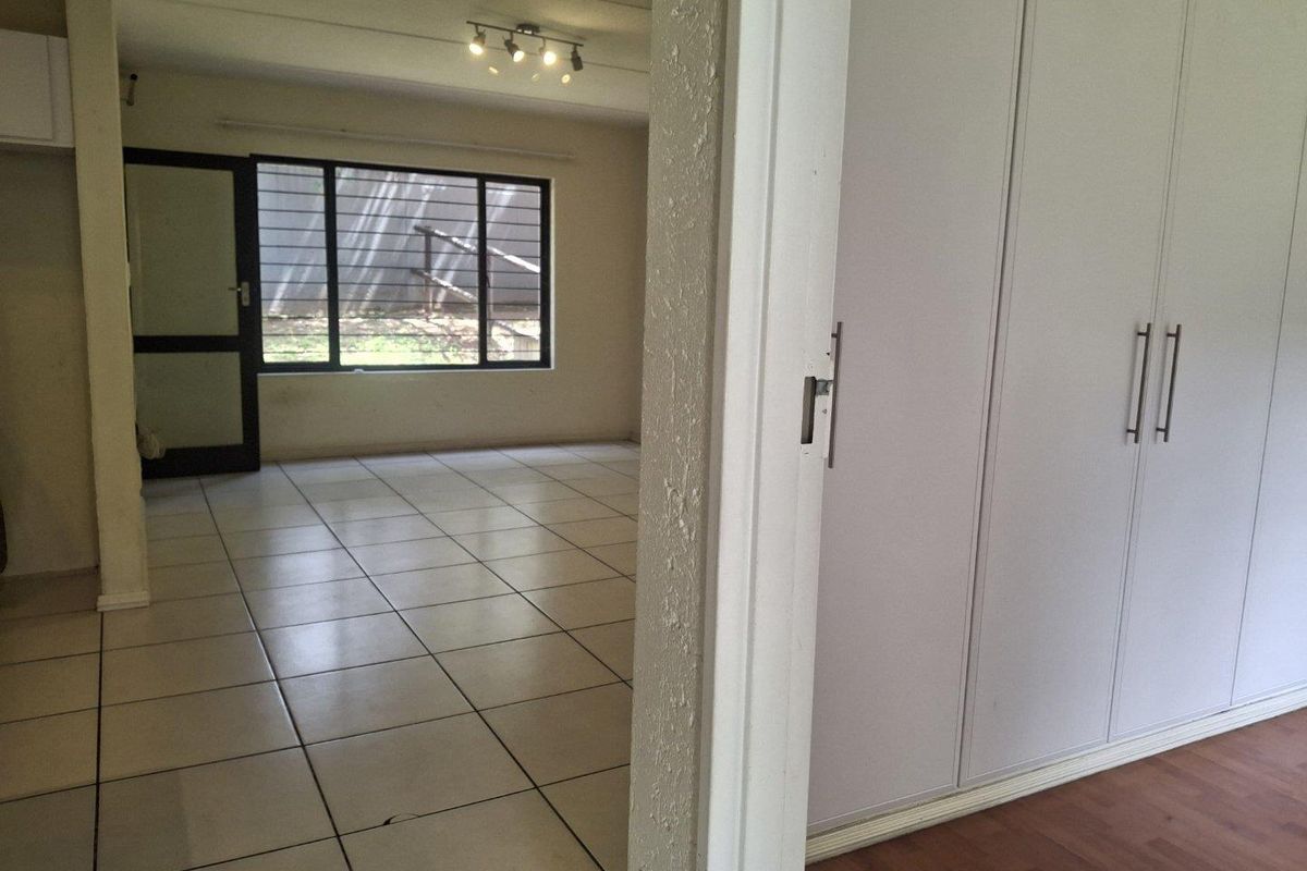 An empty living area featuring tiled floors, built-in storage cupboards, and large windows, providing a blank canvas for interior design.