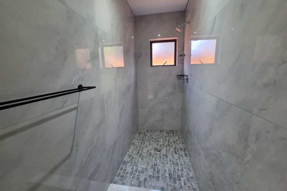 A modern walk-in shower featuring marble-look wall tiles, mosaic floor tiling, a black towel rail, and a frosted glass window.