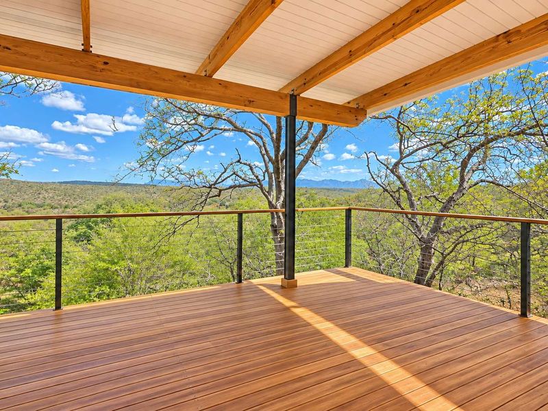 A spacious elevated timber deck featuring a covered roof structure, steel supports, and wire balustrade, offering expansive views of the surrounding natural landscape.