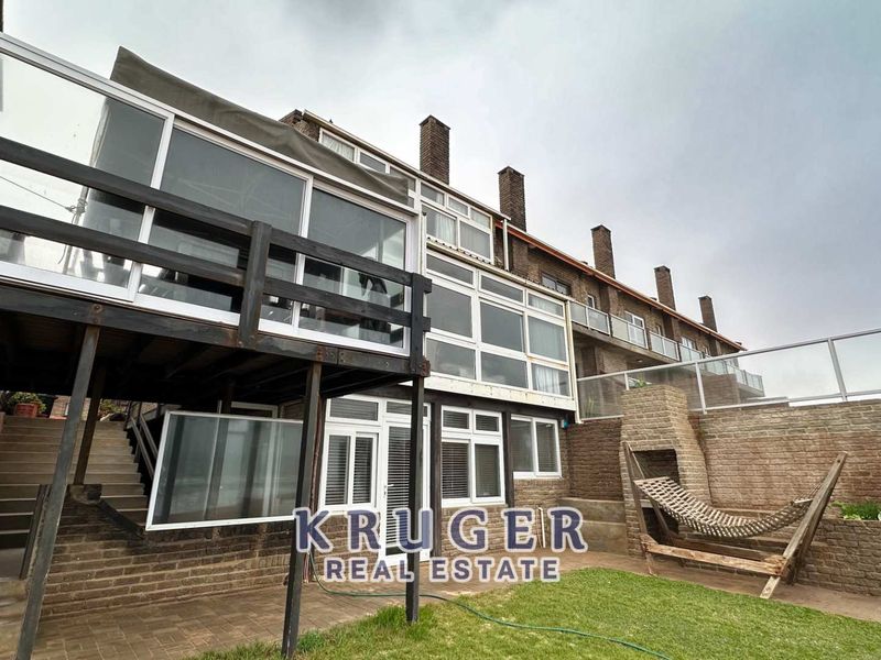 Rear elevation of a multi-level townhouse featuring a raised timber deck, paved patio area, and brick retaining walls.