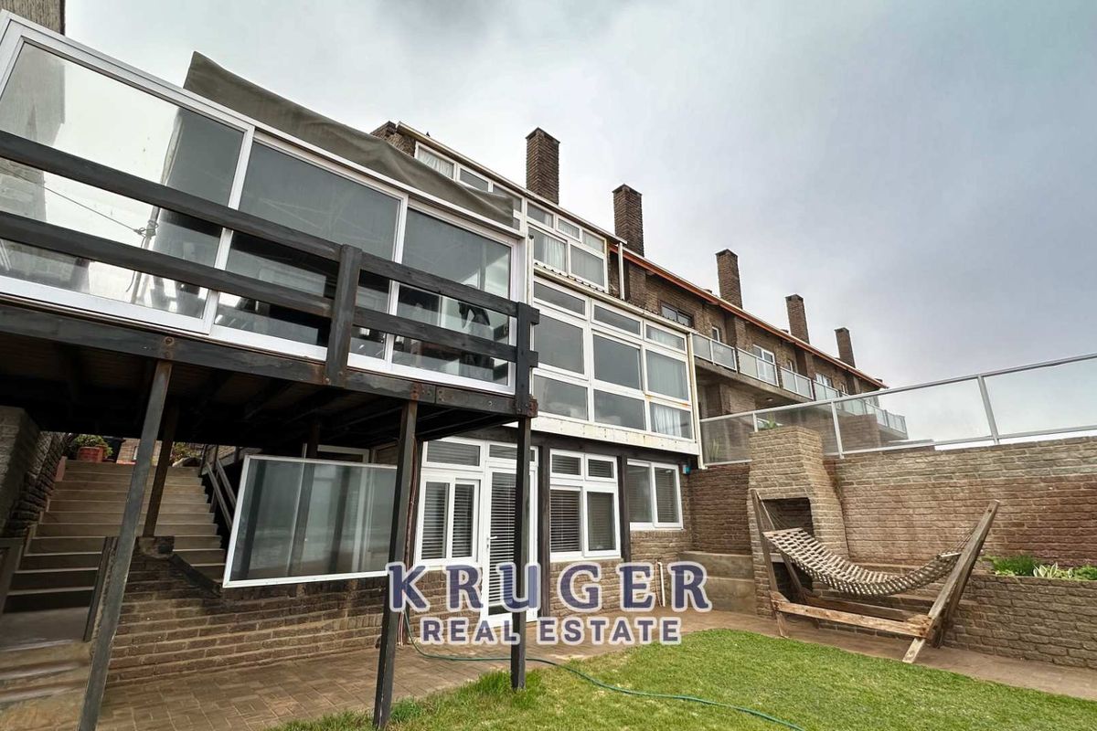 Rear elevation of a multi-level townhouse featuring a raised timber deck, paved patio area, and brick retaining walls.