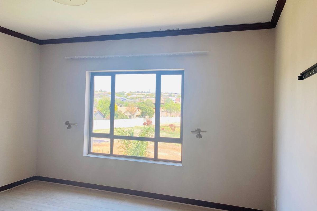 A bright, empty bedroom featuring light-toned laminate flooring, dark trim accents, and a large window providing natural light and neighborhood views.
