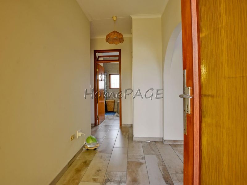 A clean, neutral-toned hallway featuring tiled flooring, an arched transition, and a wooden door frame leading to an adjacent room.