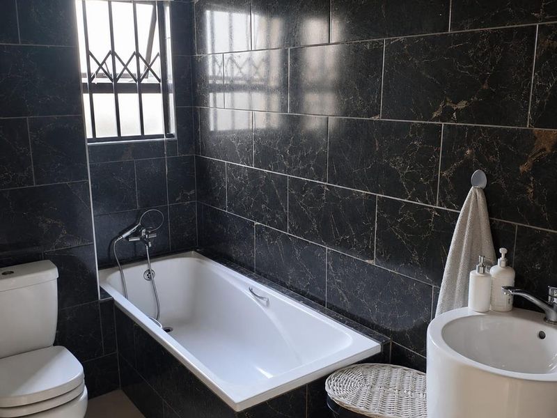 Modern bathroom featuring dark marble-effect wall tiles, a built-in bathtub with handheld shower, a pedestal basin, and a toilet.