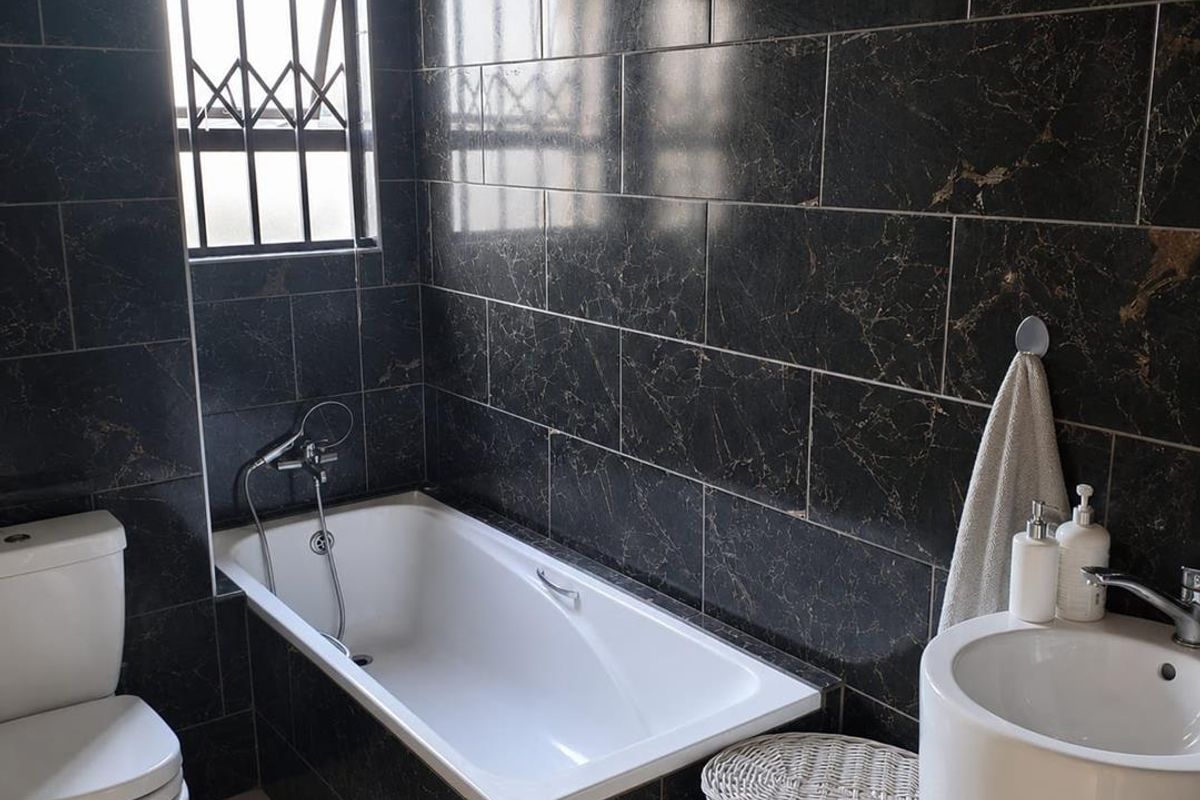 Modern bathroom featuring dark marble-effect wall tiles, a built-in bathtub with handheld shower, a pedestal basin, and a toilet.