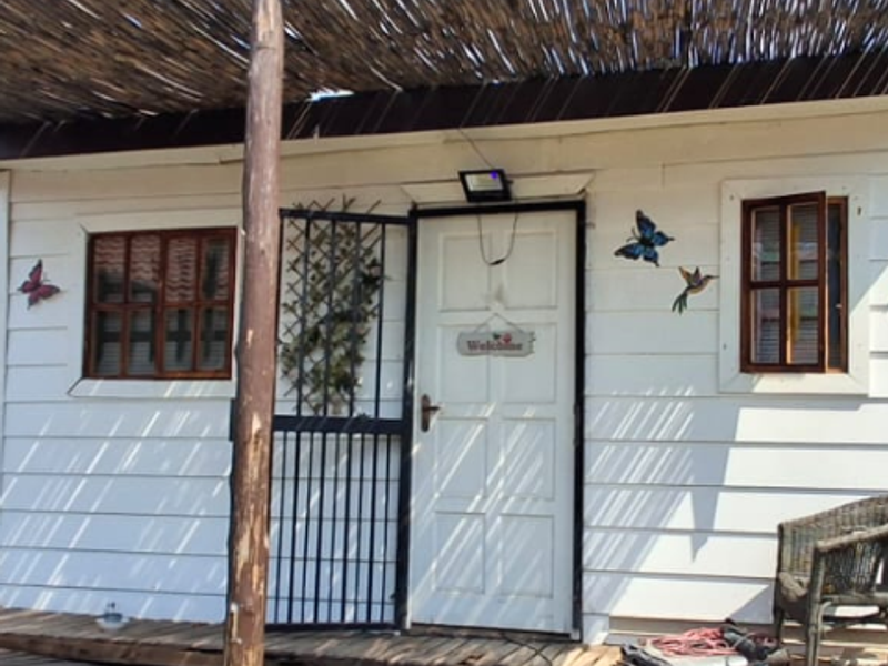 A covered patio area featuring timber decking and a rustic thatch roof, showing signs of wear and structural unevenness in the flooring.