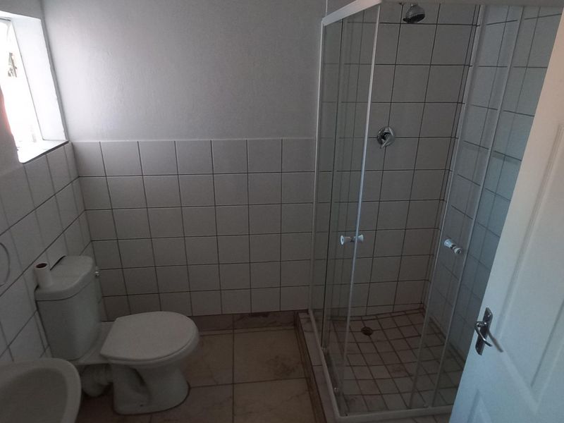 A functional bathroom featuring a glass-enclosed shower, toilet, and washbasin with neutral wall and floor tiling.