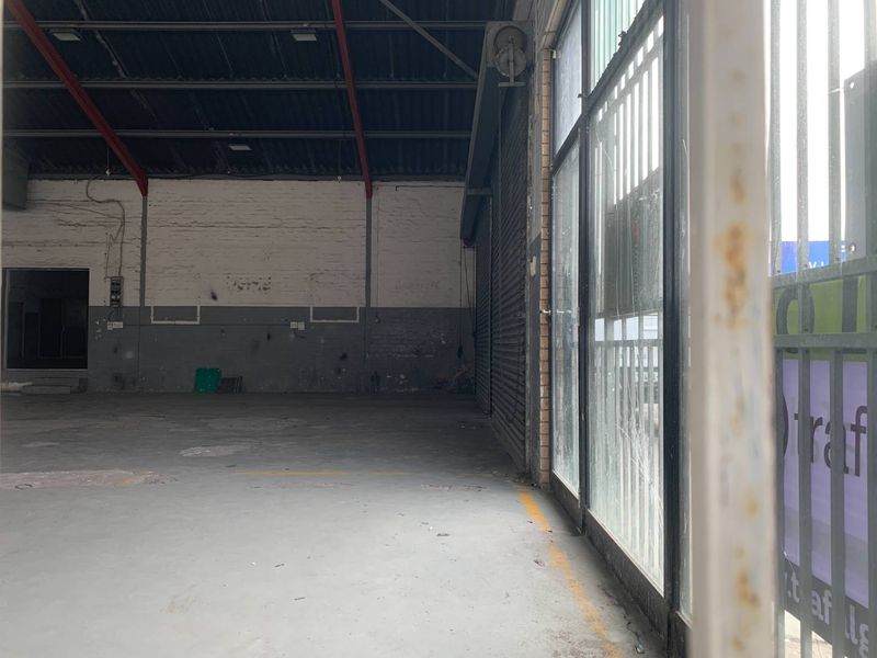 Spacious industrial utility area featuring concrete flooring, exposed steel roof trusses, and a large roller shutter door with integrated security gate.