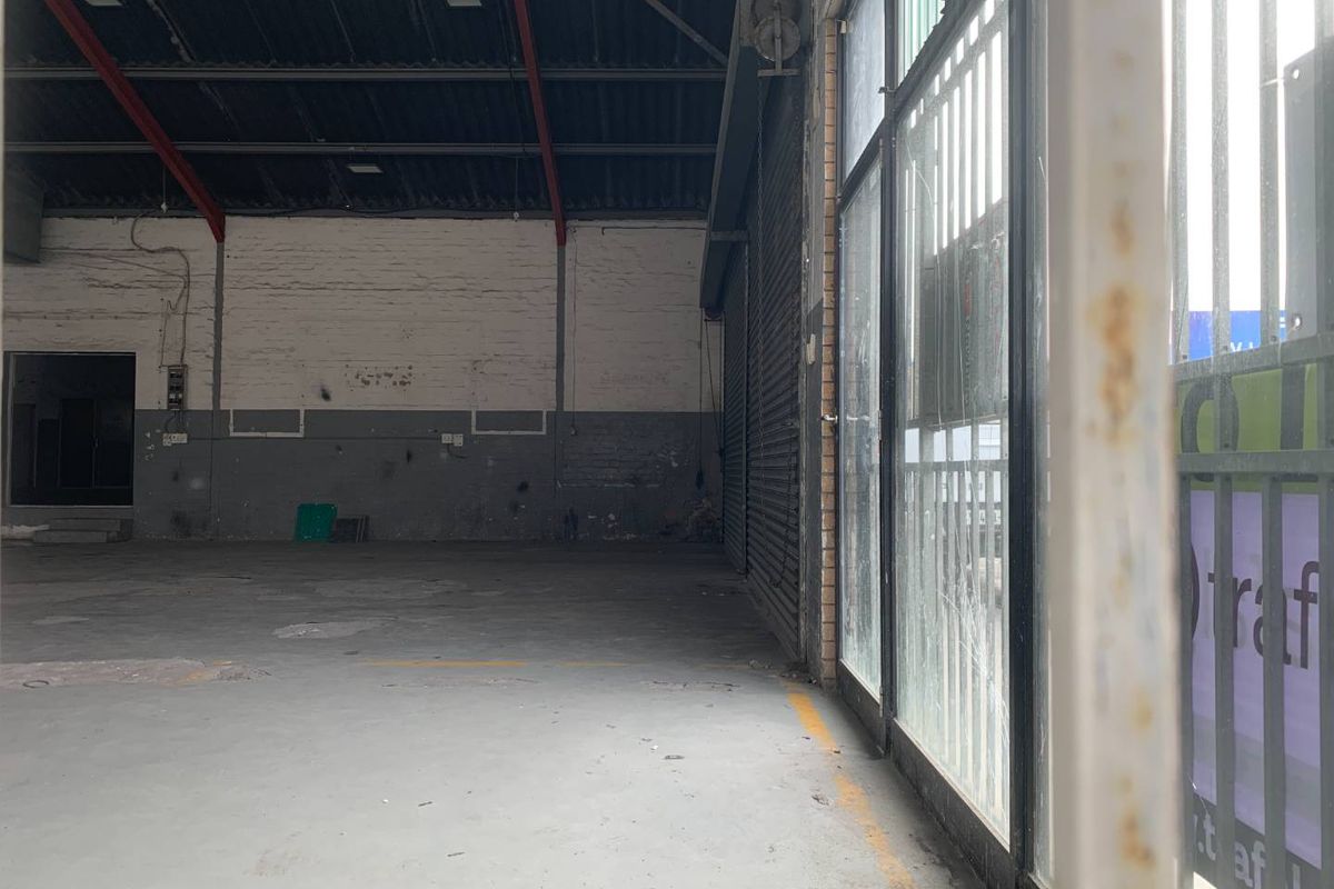 Spacious industrial utility area featuring concrete flooring, exposed steel roof trusses, and a large roller shutter door with integrated security gate.