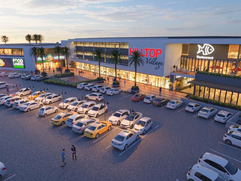 Aerial view of the Hilltop Village commercial center, featuring a large paved parking area and modern retail building facades at dusk.