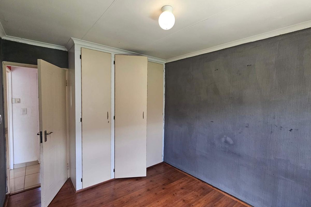 A bedroom featuring dark grey painted walls, laminate wood flooring, and built-in cupboards with cream-colored doors.