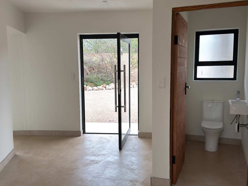 Modern entrance area featuring polished concrete flooring, a contemporary pivot front door, and an adjacent guest bathroom with clean, minimalist fixtures.