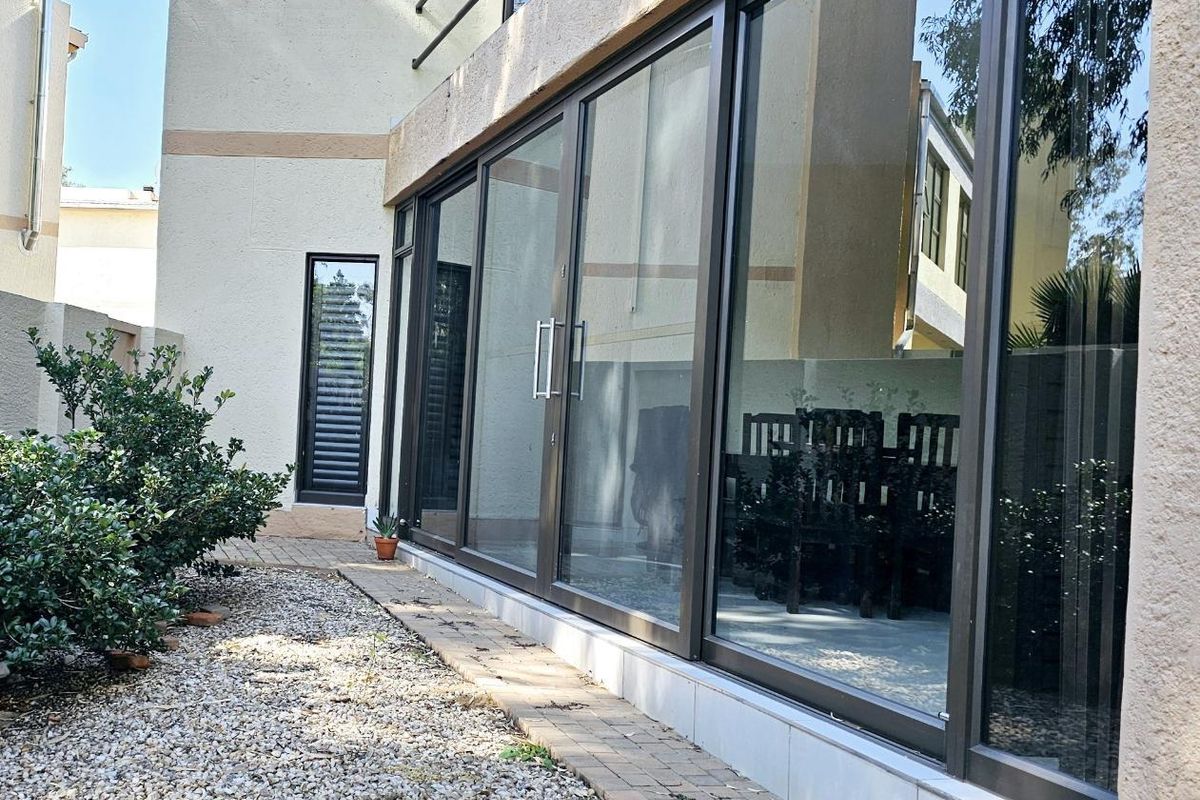 Rear exterior view of the townhouse featuring large sliding glass doors, paved walkway, and gravel garden area.