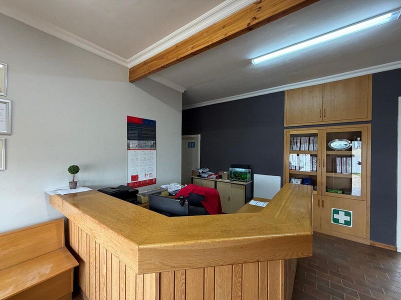 Office reception area featuring a large built-in wooden desk, integrated storage cabinetry, exposed timber ceiling beams, and durable tiled flooring.