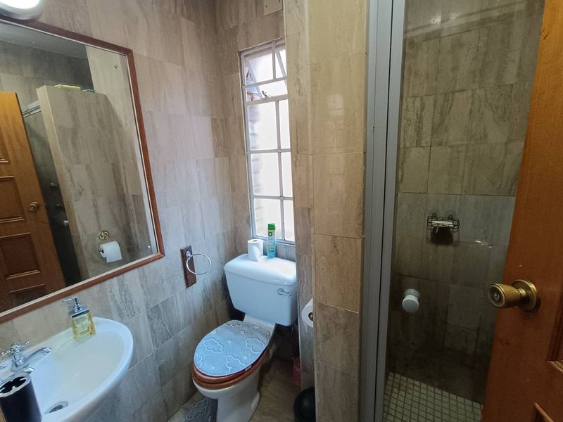 A compact bathroom featuring a pedestal basin, toilet, and a separate shower enclosure with neutral wall and floor tiling.