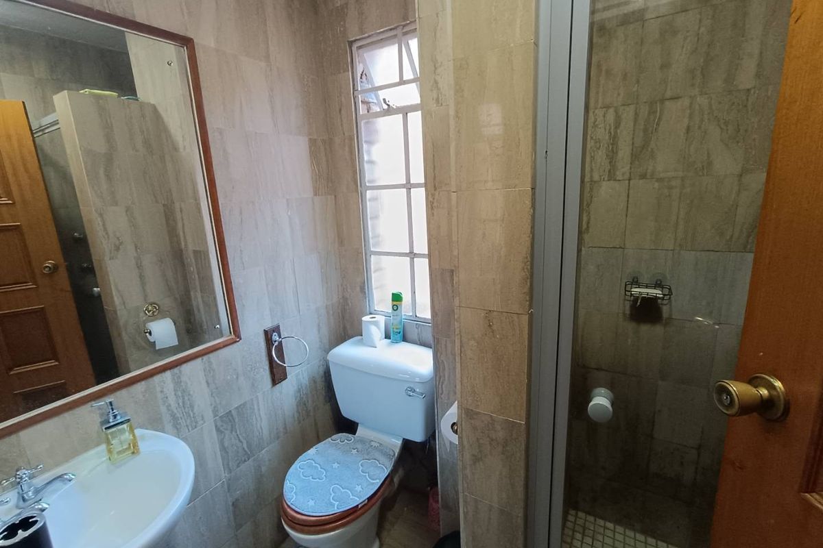 A compact bathroom featuring a pedestal basin, toilet, and a separate shower enclosure with neutral wall and floor tiling.